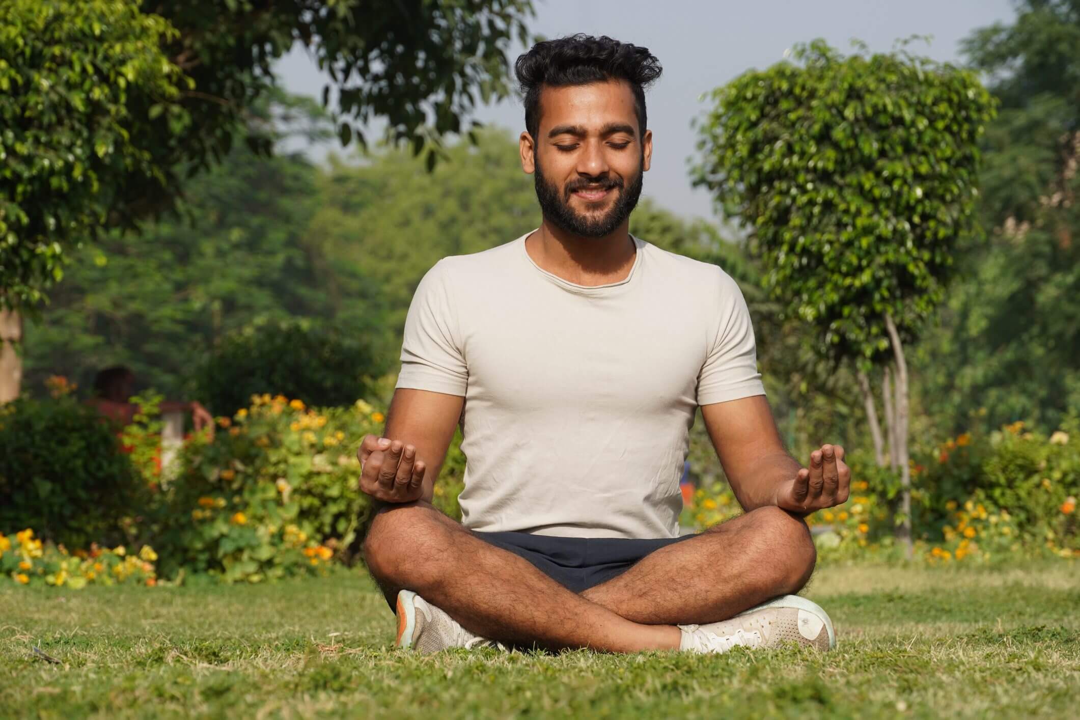 Man meditating outdoors in a garden, sitting cross-legged with eyes closed.