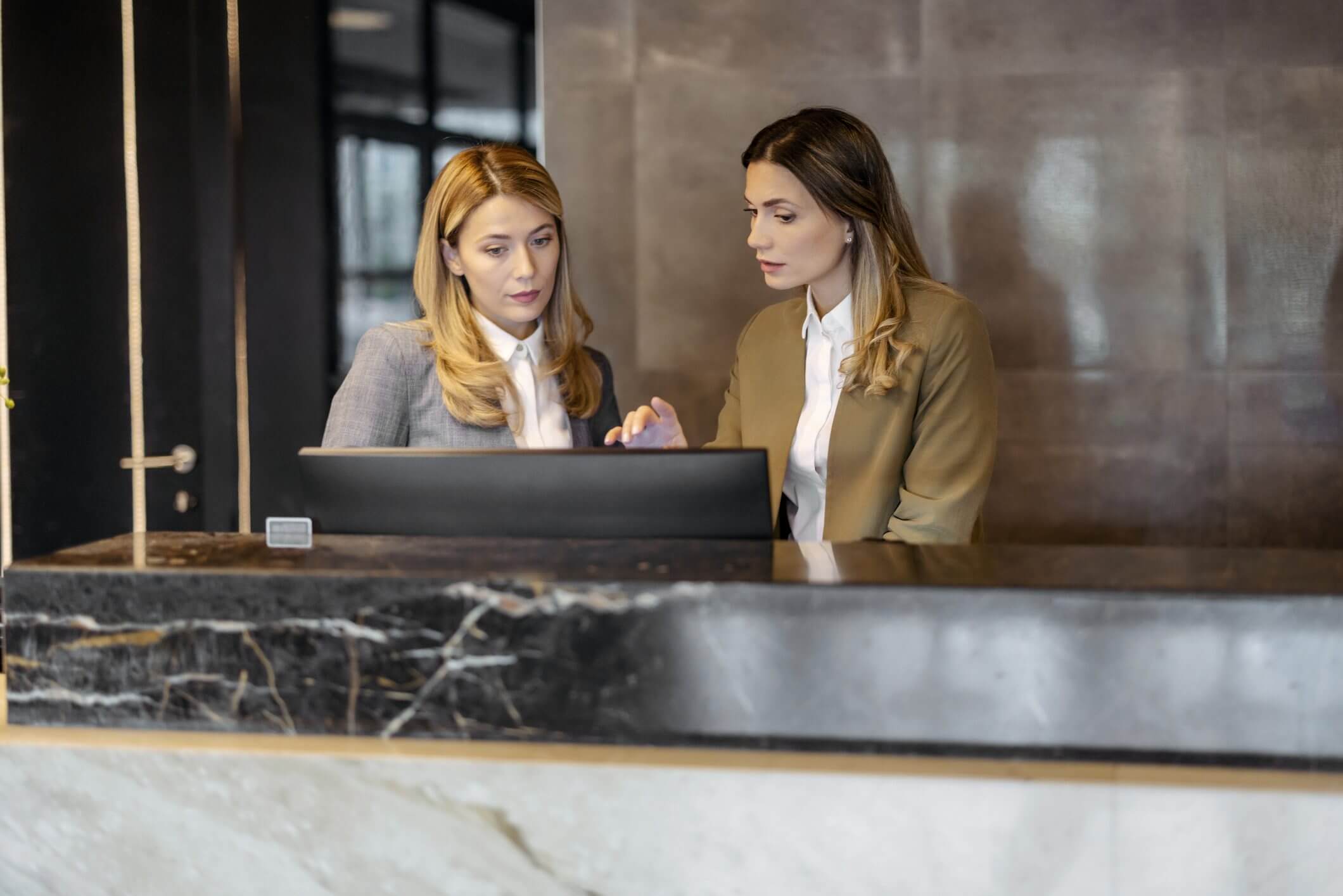Two professional women collaborate at a laptop in a modern office.